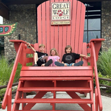 Three children sitting on 10' Giant Chair red with 'Great Wolf Lodge' sign in the background.
