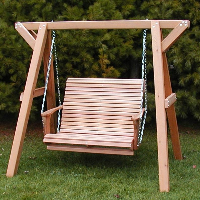 Wooden swing set with a bench seat on a grassy area with trees in the background