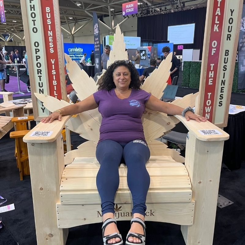 Woman sitting on Marijuandack Giant with promotional signs at a convention center.