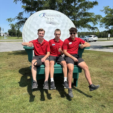Three individuals in red shirts sitting on a large green bench with a visible logo in the background.