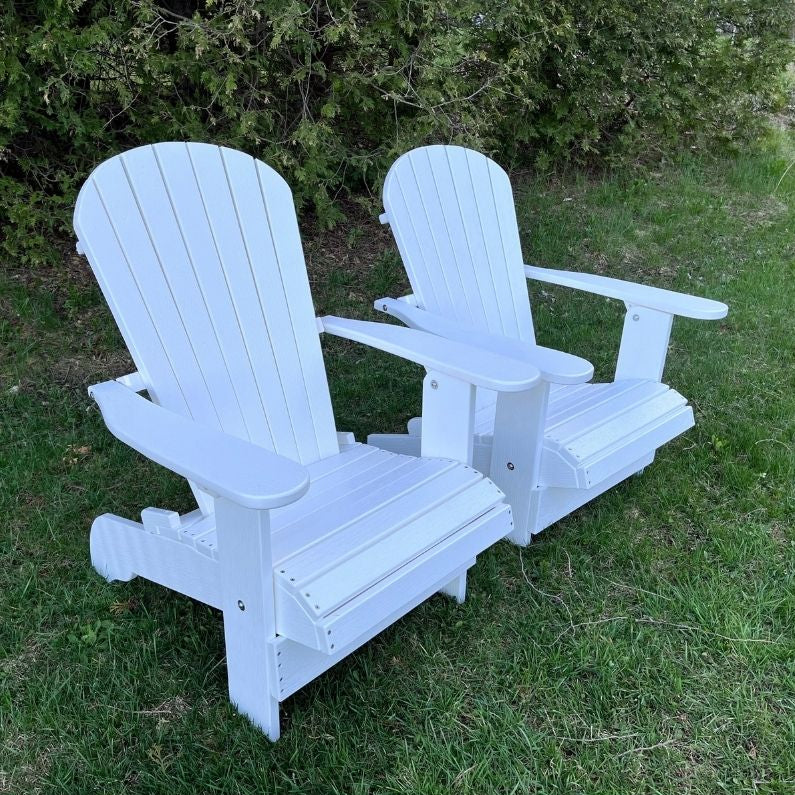 Two white Royal Upright Adirondack Chair, on grass with greenery in the background
