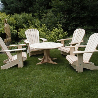 Wooden Adirondack chairs around a round table on a grassy area with greenery in the background.