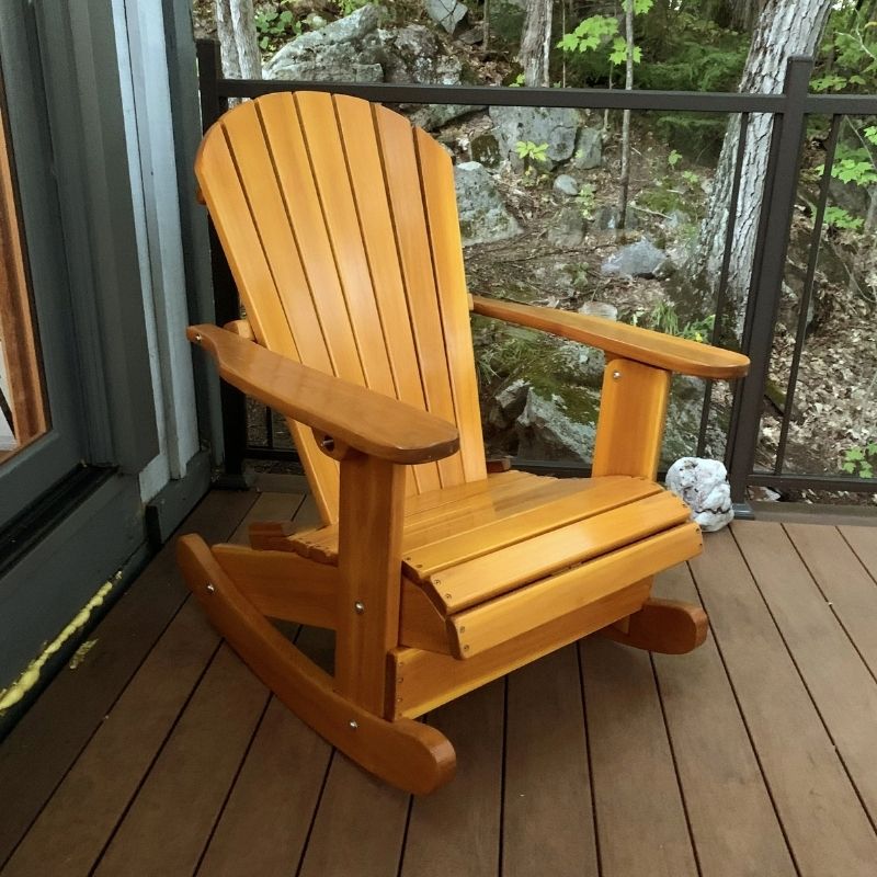 Royal Rocking Adirondack Chair (Large) on a wooden deck with a view of rocks and trees.