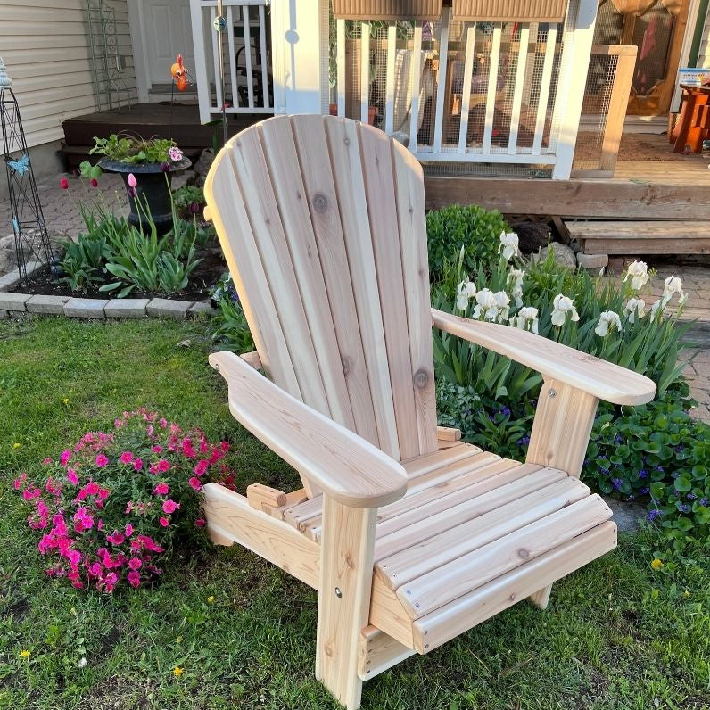 Royal Upright Adirondack Chair, in a garden setting with flowers and a deck in the background.