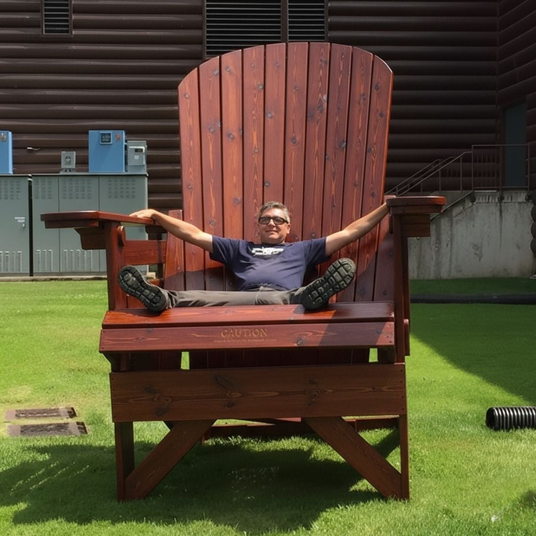 Person sitting on a large wooden chair outdoors with a building in the background