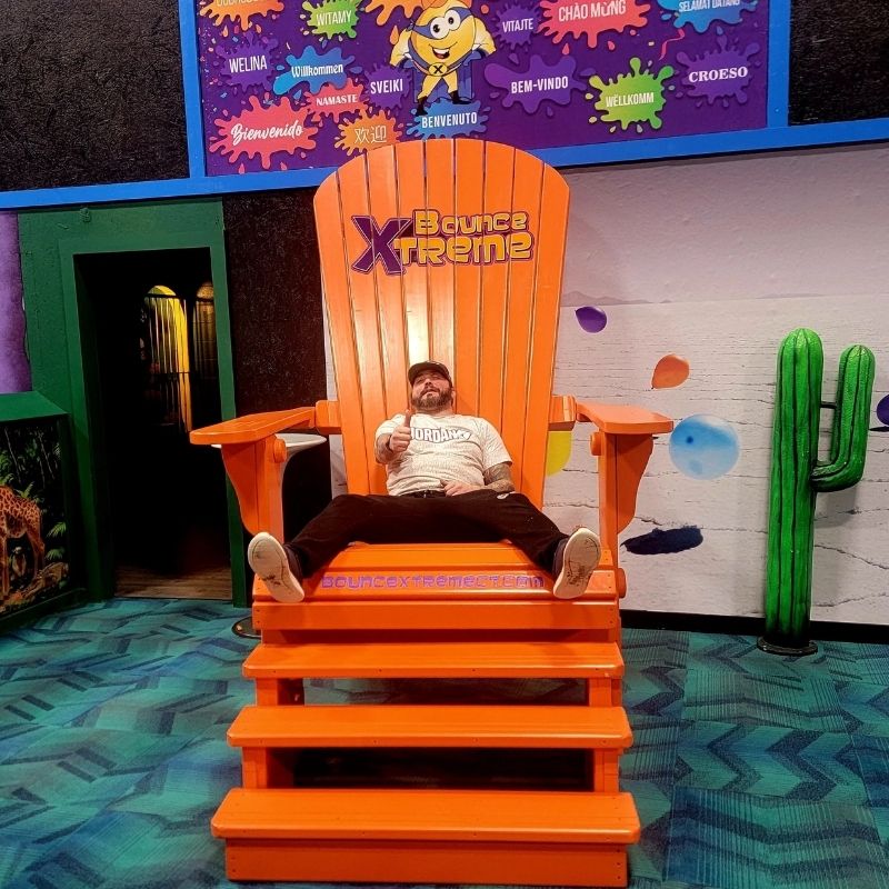 Person sitting on Traditional Giant orange chair with 'Bounce Xtreme' branding in a colorful indoor setting.