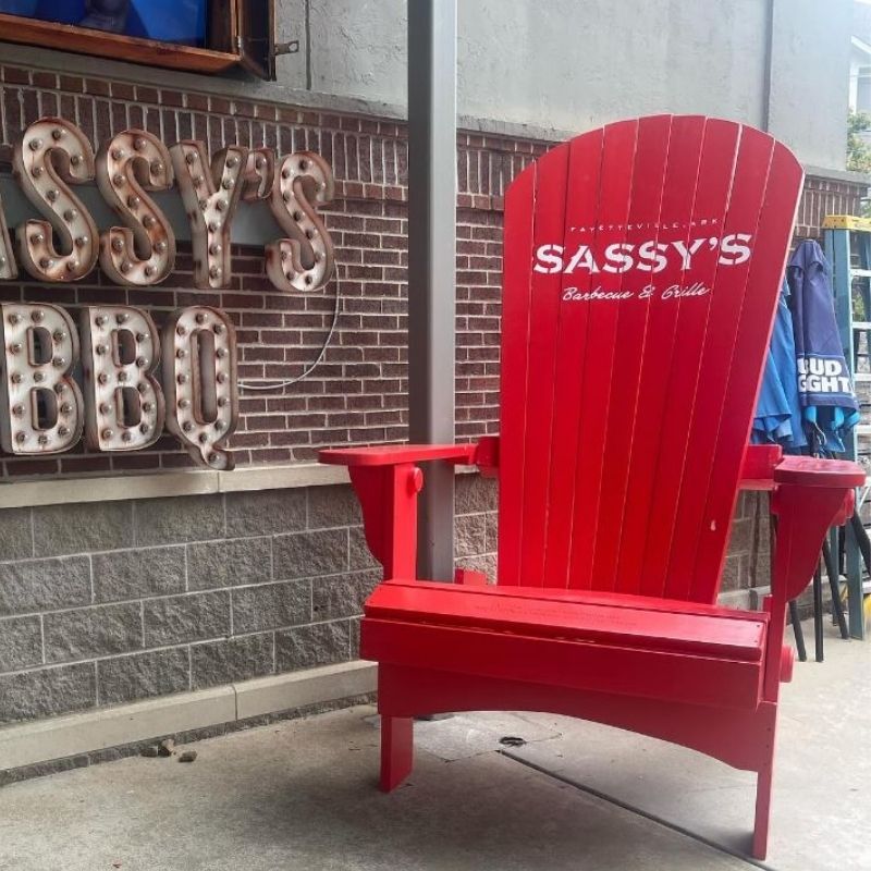 Red Traditional Giant chair with 'Sassy's' branding in front of a brick wall with 'Sassy's BBQ' sign.