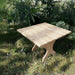 24" Square Side Table in a natural outdoor setting with greenery - clear cedar - golden glossy in a natural setting with greenery - poly luxe - woodgrain birchwood