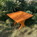24" Square Side Table in a natural outdoor setting with greenery - clear cedar - golden glossy in a natural setting with greenery - poly luxe - orange