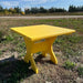Yellow wooden table in a grassy outdoor area with trees in the background