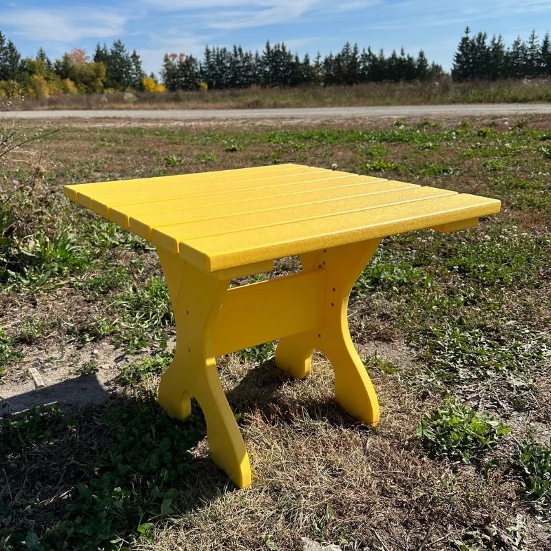 Yellow wooden table in a grassy outdoor area with trees in the background