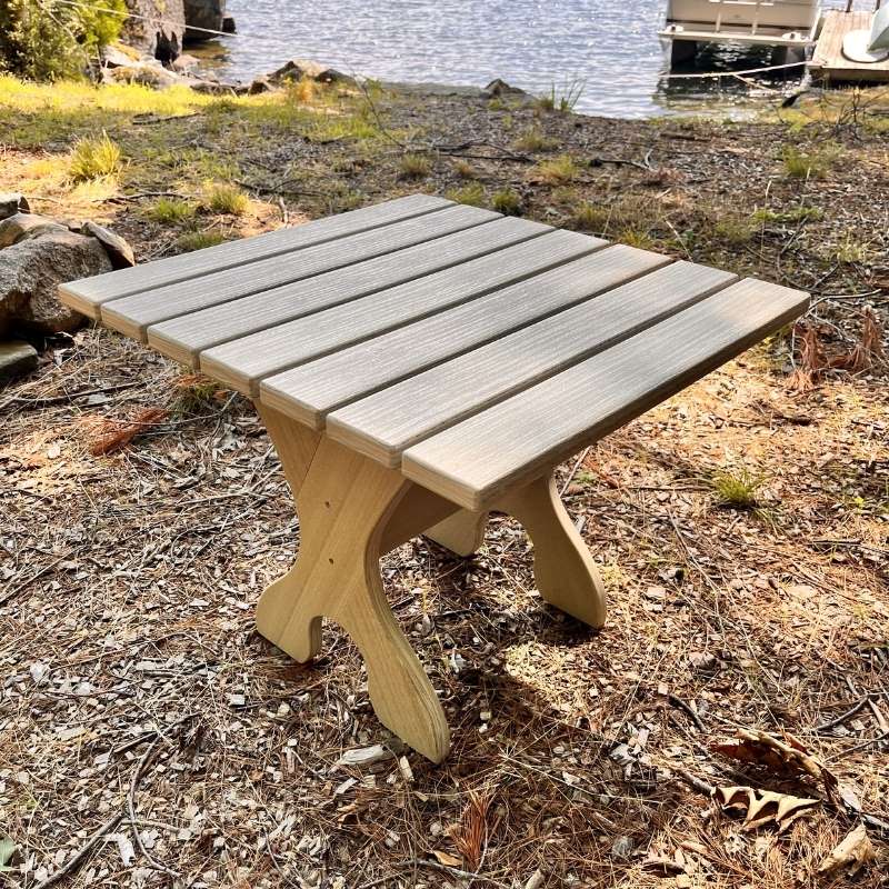 Wooden picnic table by a body of water with grass and rocks in the background
