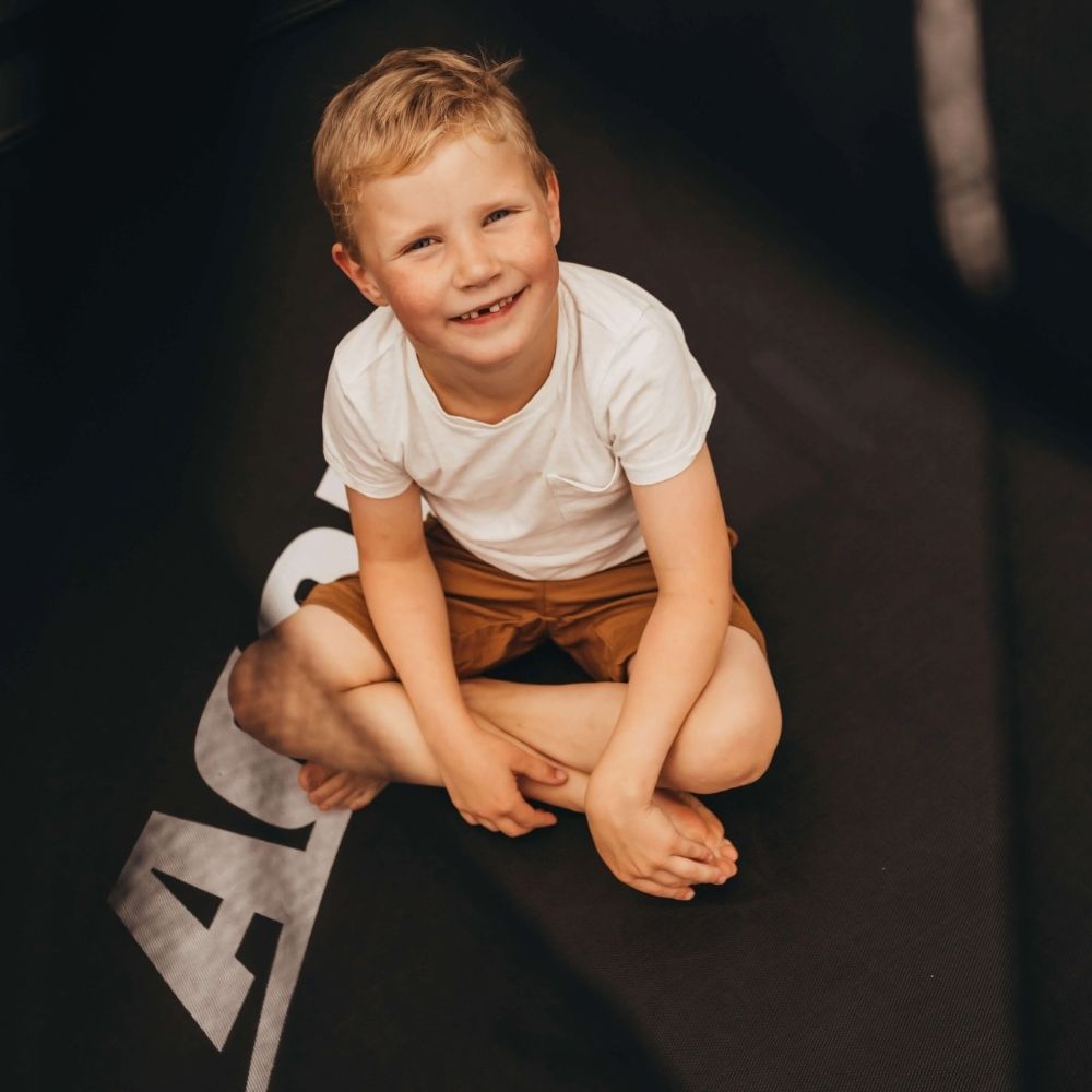 A laughing boy sits on an Acon trampoline.