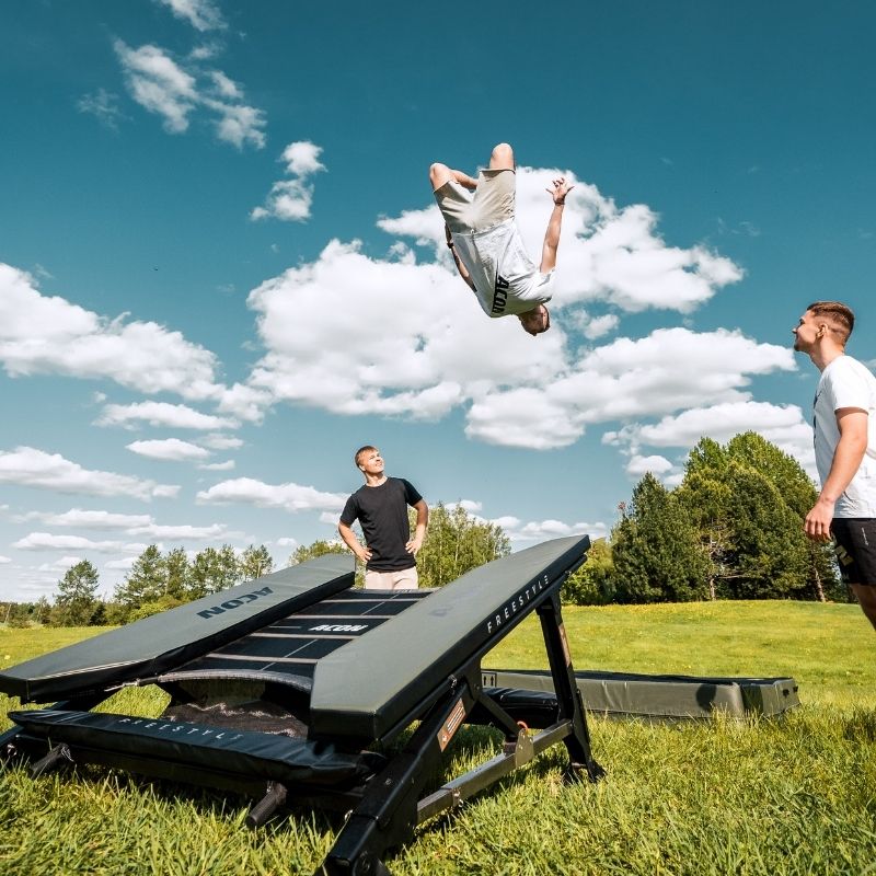 ACON Freestyle Mini Trampoline - Man performing a flip off a trampoline in an open field with a clear sky.
