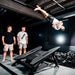 ACON Freestyle Mini Trampoline - Man performing a flip on an acrobatic platform with two observers watching 