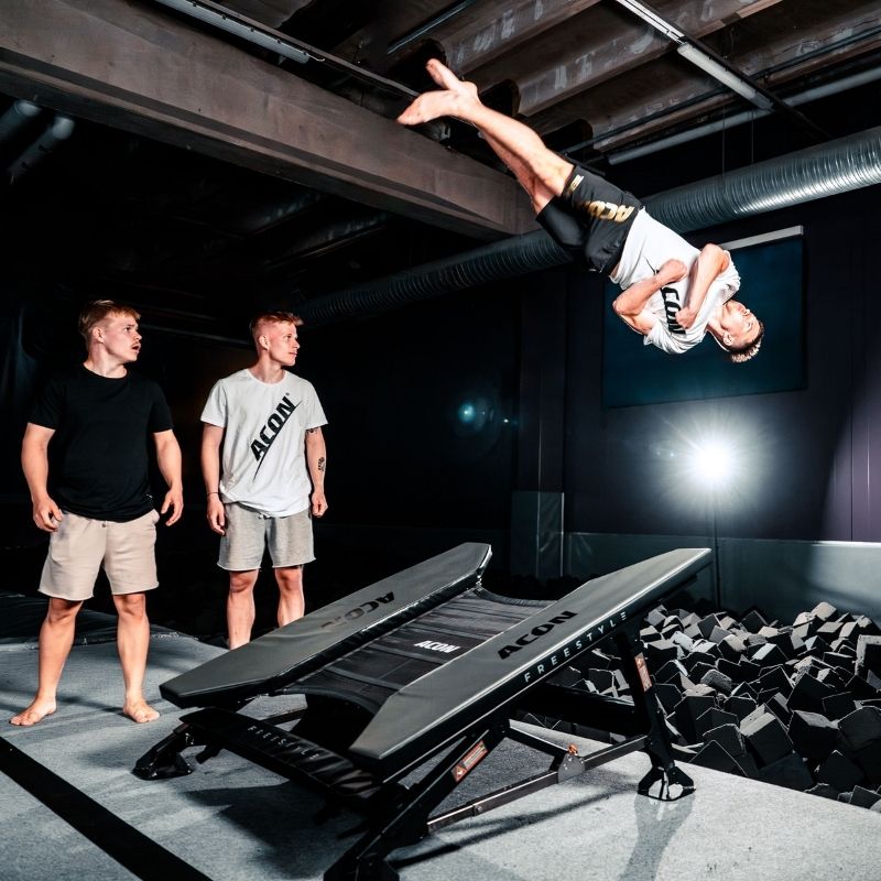 ACON Freestyle Mini Trampoline - Man performing a flip on an acrobatic platform with two observers watching 