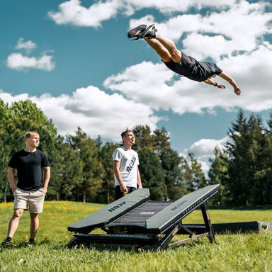 ACON Freestyle Mini Trampoline - Man performing a flip off a trampoline in an outdoor setting with trees and blue sky.