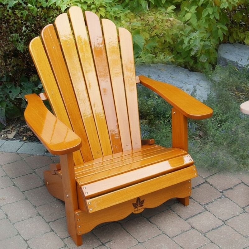 Wooden Adirondack chair on a patio with greenery in the background - scallop back  golden glossy - clear cedar