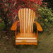Wooden Adirondack chair on a patio with greenery in the background - sandal back  golden glossy - clear cedar