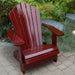 Wooden Adirondack chair on a patio with greenery in the background - scallop back  mahogamy glossy - clear cedar