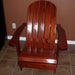 Wooden Adirondack chair on a patio with greenery in the background - flat back  mahogany glossy - knotted cedar