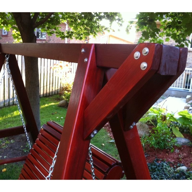 Red swing set in a backyard with green grass and trees.
