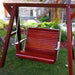 Red wooden swing in a garden setting with greenery and a house in the background