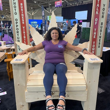 Woman sitting on Marijuandack Giant with promotional signs at a convention center.