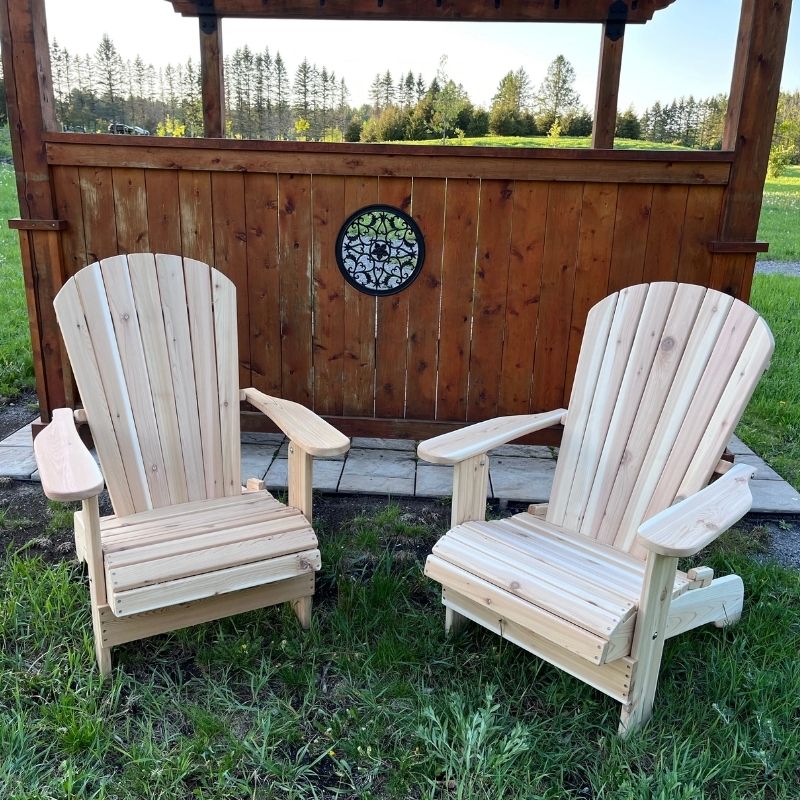 Two Royal Upright Adirondack Chair, in front of a wooden structure with a scenic background.