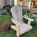 Royal Upright Adirondack Chair, in a garden setting with flowers and a deck in the background.