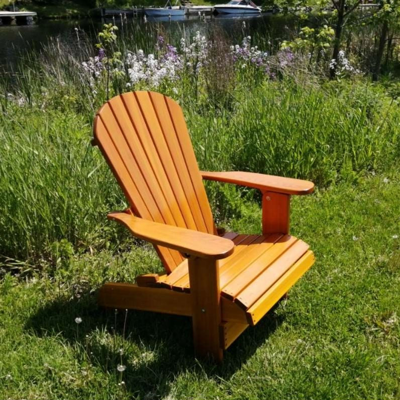 Royal Upright Adirondack Chair, in a grassy area with a lake and boats in the background